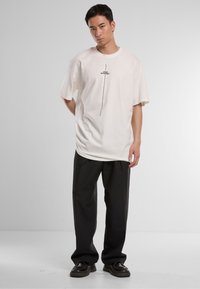 Cream oversized t-shirt with a central black graphic text "THINK DIFFERENT." Black wide-leg trousers and black shoes. Smooth texture.