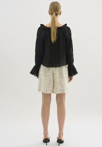 Schwarzes Off-Shoulder-Oberteil mit gerafftem Kragen, kombiniert mit weißen Shorts mit vertikalen schwarzen Streifen, von hinten betrachtet.