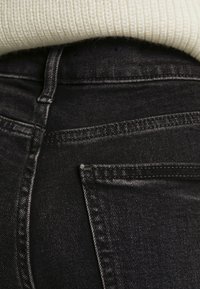 Jeans de mezclilla negra con una textura suave, que presentan un bolsillo lateral y un acercamiento a los detalles de la costura cerca de la cinturilla.