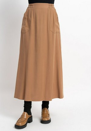 Beige knöchellange Rock mit tailliertem Bund, seitlichen Taschen und glattem Stoff. Kombiniert mit braunen Slippern und schwarzen gepunkteten Socken.