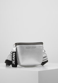 Borsa a spalla metallica argentea con chiusura a zip, caratterizzata da una superficie testurizzata e una tracolla nera con l'etichetta "JEANS" per un tocco di stile in più.