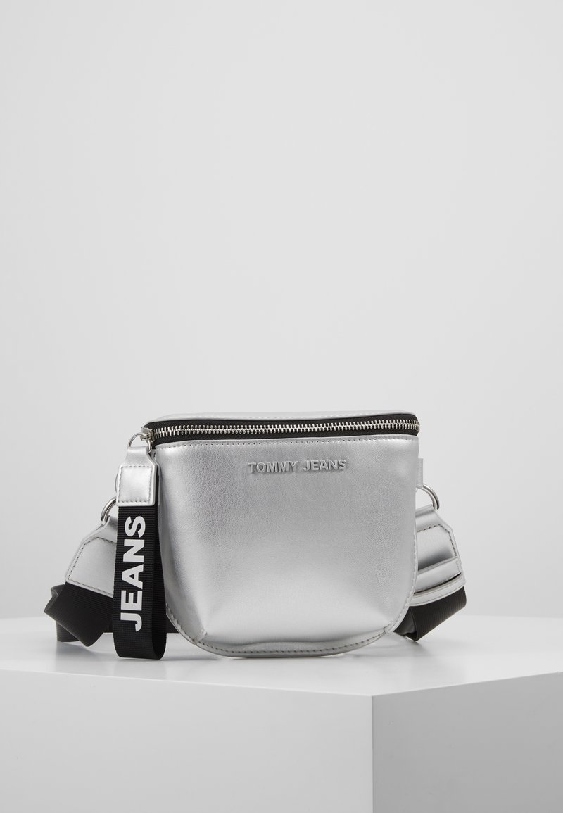 Borsa a spalla metallica argentea con chiusura a zip, caratterizzata da una superficie testurizzata e una tracolla nera con l'etichetta "JEANS" per un tocco di stile in più.
