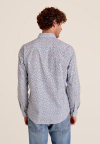 Lichtblauw hemd met lange mouwen, voorzien van een multicolore bloemenpatroon, een button-down kraag en een gebogen zoom. Zichtbare manchet en stikseldetails.