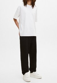 Biały bawełniany t-shirt z krótkim rękawem w zestawie z czarnymi dresami i białymi trampkami. Prosty, luźny krój bez wzorów i ozdób.