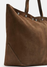 Bruine suedine totebag met zwarte leren handvatten en zilveren klinknageldetails langs de bovenrand.