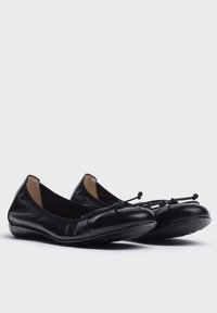 Bailarinas de cuero negro con punta redonda, bordes elásticos, acento de lazo delgado en la parte frontal y suela de goma flexible. Textura suave.