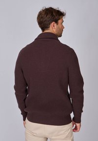 Pull en laine tricoté brun foncé avec un col châle, texture côtelée et manches longues. Présente un ourlet inférieur ajusté et des détails texturés.