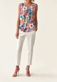 Top sin mangas floral en azul, rosa y verde; combinado con pantalones blancos ajustados y sandalias de tacón alto rosas con tiras.