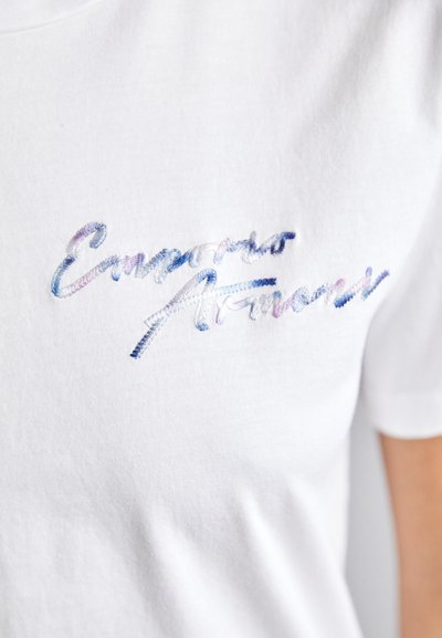 Weißes Baumwoll-T-Shirt mit mehrfarbig gesticktem Text "Emperio Armani" in einer geschwungenen Schriftart, zeigt eine glatte Stofftextur.