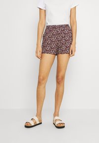 Purple patterned shorts with a smocked waist, paired with a white short-sleeve t-shirt and beige platform sandals with cork soles.