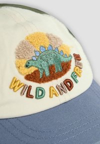 Baumwollmütze mit gelblicher Vorderseite, bestickt mit einem grünen Stegosaurus und buntem Schriftzug "WILD AND FREE", blauer Stoffschirm.