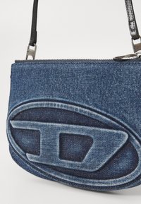 Borsa a tracolla in denim con un design ovale testurizzato. Presenta una chiusura con zip e una tracolla nera, con una palette di colori blu.