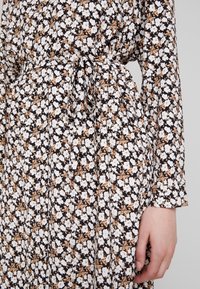 Blommönstrad klänning i svart, med vita och ljusbruna blommor. Långa ärmar, midjeband och flödande textur.