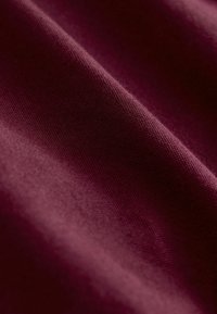 Tissu bordeaux profond avec une texture de tissage fin visible et des plis lisses créant des ombres douces et des reflets.