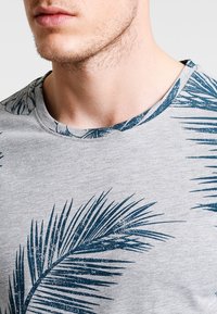 Grå bomulds T-shirt med rund halsudskæring, prydet med et blåt palmebladmotivet og en tekstureret overflade. Casual og kortærmet design.