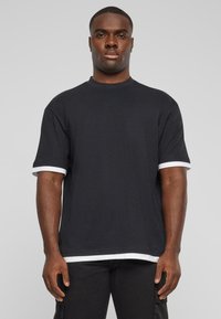 Sort t-shirt med korte ærmer og hvide manchetter. Lavet af bomuld med en afslappet pasform og rund halsudskæring, med en lige kant.