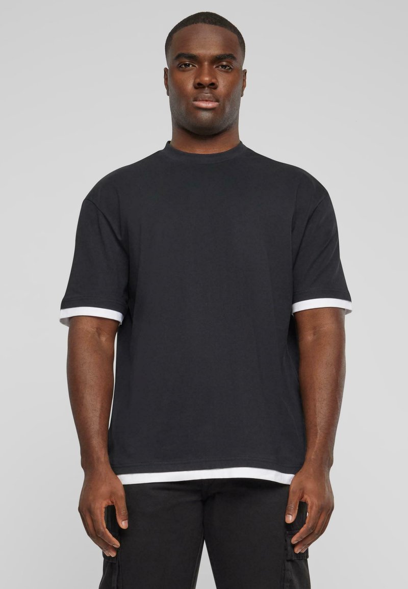 Sort t-shirt med korte ærmer og hvide manchetter. Lavet af bomuld med en afslappet pasform og rund halsudskæring, med en lige kant.