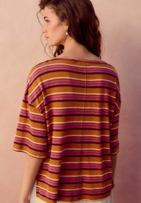 Gestreiftes Oberteil mit horizontalen Linien in Gelb, Pink und Lila. Lockerer Schnitt mit kurzen Ärmeln, gefertigt aus weichem, strukturiertem Stoff.