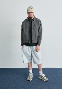 Gray cotton jacket with a front pocket, black T-shirt, light blue shorts, and gray sneakers with white accents and laces. Beige cap with text.
