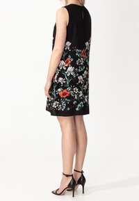 Schwarzes ärmelloses Kleid mit einem floralen Muster in Rot, Weiß und Grün. Kurze Länge mit einem Schlüsselloch-Ausschnitt hinten und einer glatten Textur.