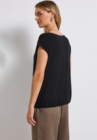 Svart kortärmad topp i mjukt tyg, med en lös design och rundad halsringning samt något gatherad nederkant.