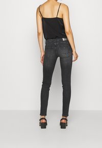 Top negro sin mangas combinado con unos pantalones ajustados grises oscuros. Los pantalones presentan un diseño estándar de bolsillo trasero y detalles de costura mínimos.