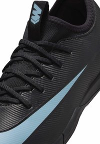 Zwarte sportschoen met een gestructureerd materiaal, contrasterende lichtblauwe swoosh en zwarte veters. Voorzien van een gevoerde kraag en een stevige zool.