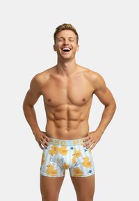 Męskie bokserki wykonane z jasnoniebieskiej tkaniny z powtarzającym się wzorem kaczek i kształtów geometrycznych. Elastyczny pas z logo „MK” w kolorze złotym.