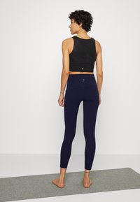 Svart cropped tanktop med strukturert stoff kombineres med høyhalsede marineblå leggings, som har en glatt overflate og en tettsittende silhuett.