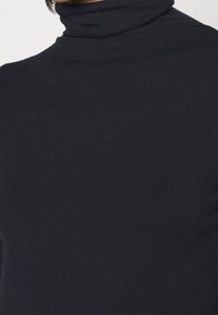 Schwarzer Rollkragenpullover mit tailliertem Design. Glattes, dehnbares Material, das sich dem Körper anpasst, mit einem hohen Kragen.
