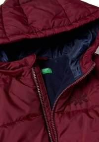 Vínová prošívaná bunda s kapucí, s prošívanou texturou, tmavě modrou vnitřní podšívkou a zelenou značkovou etiketou u zipu.