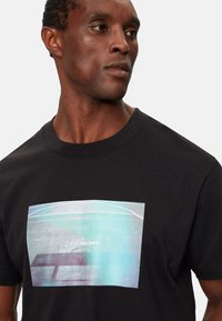 Camiseta de algodón negra con un gráfico centrado en suaves tonos de azul y blanco, con el texto "Calvin Klein Jeans" debajo. Mangas cortas, cuello redondo.