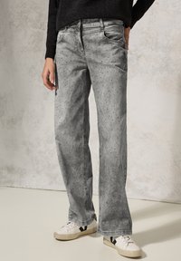 Grijze denim jeans met een relaxte pasvorm, voorzien van lichte slijtage en kleine studdetails. Draagt met witte sneakers.