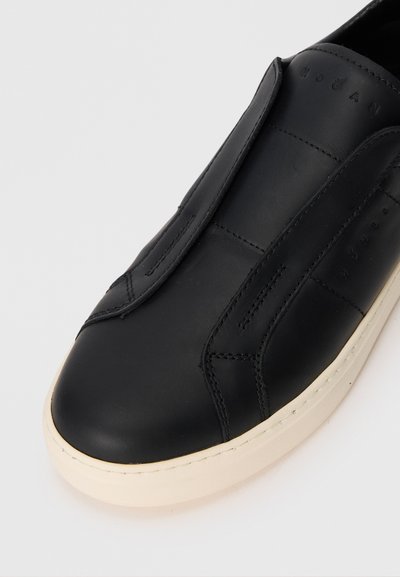 Pantof de piele neagră, slip-on, cu o textură netedă, având vârful rotund și accente cusute. Talpa din cauciuc alb cu un design discret.