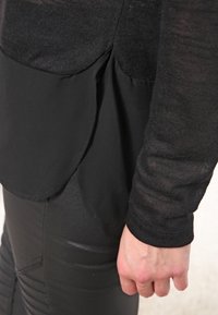 Schwarzes, geschichtetes Oberteil, das im oberen Bereich aus einem durchsichtigen Strickstoff besteht und im unteren Bereich aus einem glatten, matten Stoff. Der Saum hat abgerundete seitliche Akzente.