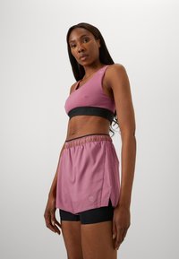 Athletic outfit featuring a pink sports bra with black band and matching pink shorts over black compression shorts, showcasing a sleek design.