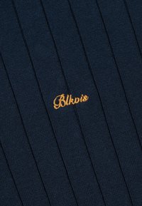 Tissu tricoté côtelé bleu foncé avec un petit texte jaune brodé "Blkpio" près du centre.