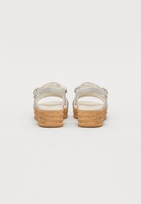 Silver strappy sandals with a textured cork-like wedge heel and cushioned footbed, featuring adjustable ankle straps for secure fit.