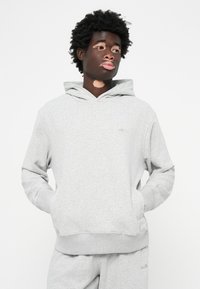 Sweatshirt cinza claro feito de um tecido suave, com um bolso canguru e punhos canelados. Marca discreta no peito.