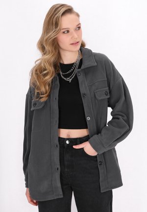Grijze fleece knoopjack met een kraag, twee voorzakken en een relaxte pasvorm, gecombineerd met een zwart top en hoge taille spijkerbroek.