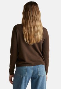 Hnědý svetr s jemnou texturou, dlouhými rukávy a volným střihem, doplněný o světle modré džíny s klasickým pětipocket designem.