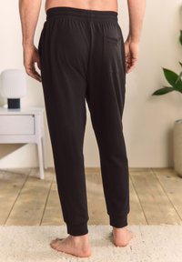 Pantaloni jogger negri dintr-un material moale, prevăzuți cu talie elastică și o buzunar în spate, conici spre gleznă cu manșete ribate.