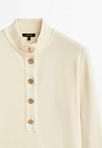 Maglione a coste color crema con colletto alto e cinque bottoni decorativi dorati lungo il davanti.