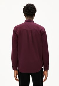 Camicia bordeaux a maniche lunghe con colletto a punta, dotata di piega sul retro e polsini con bottone. Tessuto di cotone morbido, orlo arrotondato.