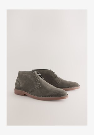 Hallid seemisnahast pahkluumadalad terava ninaosaga, millel on lihtsad nöörid, õmmeldud detailid mööda tallapoolset äärt ning pruun kummist väljatallad.