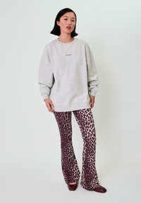 Šedá mikina s žebrovanými manžetami, doplněná rozšířenými kalhotami s odvážným vzorem z hnědých a krémových leopardích skvrn. Celkový vzhled doplňují hnědé ploché boty.