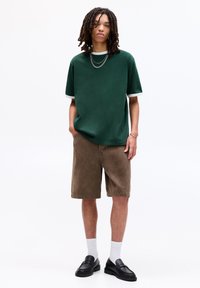 Grøn oversized kortærmet skjorte med hvid kant, parret med brune corduroy shorts. Sorte loafers og hvide sokker fuldender looket.