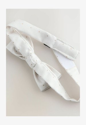 Papillon bianco texturizzato con piccoli pois beige, cinturino regolabile e chiusura a strappo su sfondo chiaro.