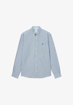 Světle modrá košile s dlouhým rukávem a límečkem na knoflíky, má bílé knoflíky a modře vyšitý logo na hrudi. Měkká struktura látky.