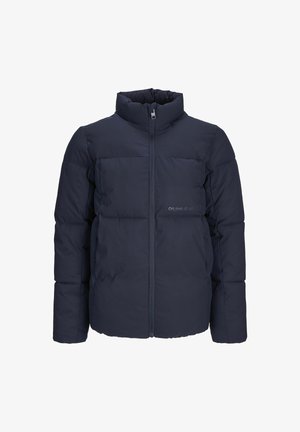 Granatowa puchowa kurtka z wysokim kołnierzem, pikowanym wzorem i przednimi kieszeniami. W zestawie z ciemnozielonym swetrem i jasnoniebieskimi dżinsami o szerokich nogawkach.